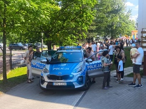 Na zdjęciu oznakowany radiowóz i osoby go oglądające. W tle tłum ludzi.