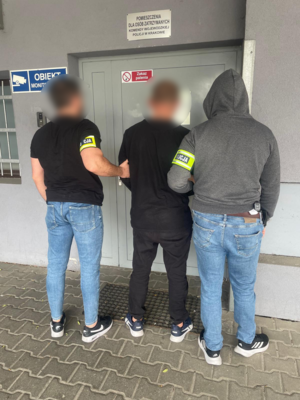 Zatrzymany mężczyzna prowadzony przez nieumundurowanych policjantów