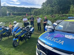 umundurowani policjanci, przed nimi motory policyjne i oznakowany radiowóz