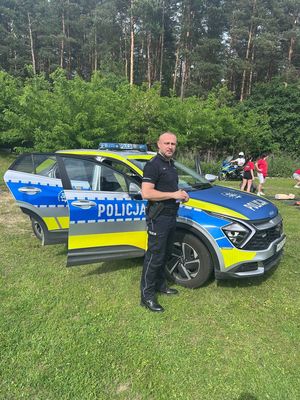 umundurowany policjant stojący przed oznakowanym radiowozem
