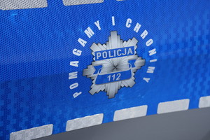 Odznaka policyjna zamieszczona na radiowozie. Wokół niej napis pomagamy i chronimy