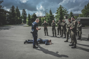 Dwóch policjantów jeden z nich lezy na ziemi drugi stoi obok wszystkiemu przygladaja się żołnierze