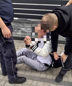 Mężczyzna w kajdankach siedzący na chodniku obok niego dwaj policjanci