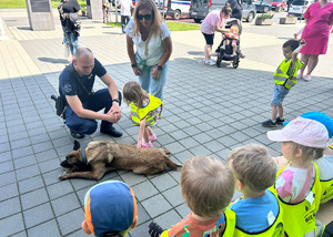 dziecko głaszcze policyjnego psa w towarzystwie przewodnika i innych osób