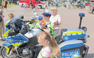 dziecko siedzi na policyjnym motocyklu obok inne dzieci i dorośli