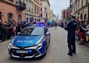 umundurowany policjant stojący przy radiowozie na jednej z ulic miasta obseruje widzów oraz uczestników Wielkiej Parady Smoków
