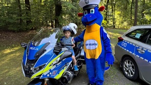 dziecko siedzi na policyjnym motocyklu obok stoi smok Bazyli przy radiowozie