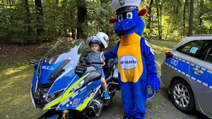 dziecko siedzi na policyjnym motocyklu obok stoi smok Bazyli przy radiowozie