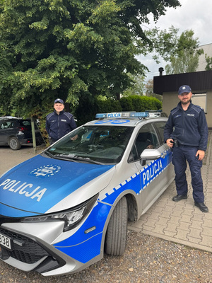 Dzielnicowi przy radiowozie  w tle drzewa