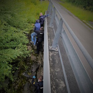 policjanci pomagają wyjść mężczyźnie z zarośli pod mostem