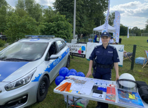 umundurowana policjantka stoi przy stoisku profilaktycznym wystawionym przez Policje koło policjantki stoi zaparkowany oznakowany radiowóz
