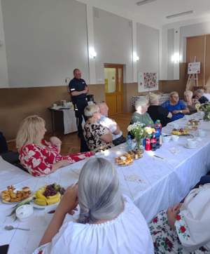 Umundurowany policjant oraz seniorzy biorący udział w akcji