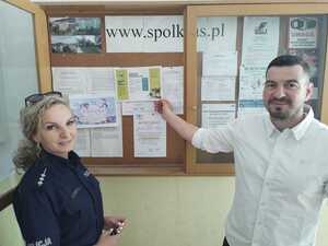 Mężczyzna wskazuje na ulotkę w gablocie. Obok stoi policjantka.