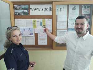 Mężczyzna wskazuje na ulotkę w gablocie. Obok stoi policjantka.