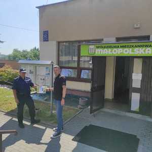 Policjant i osoba przed wejściem do spółdzielni mieszkaniowej.