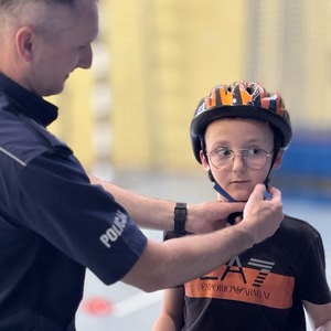 policjant poprawiający zapięcie kasku młodemu rowerzyście