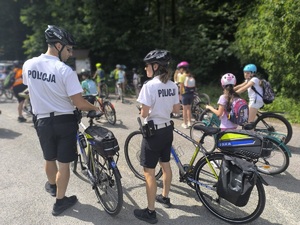Policjant i policjantka na rowerach czuwają nad bezpieczeństwem dzieci na rowerach