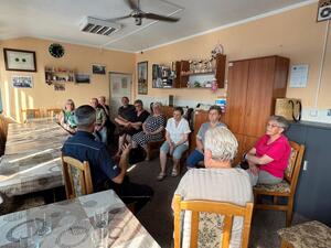Umundurowany policjant oraz siedzący na krzesłąch seniorzy