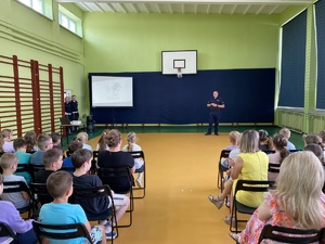 umundurowani policjanci na sali gimnastycznej podczas prelekcji przed nimi siedzą dzieci