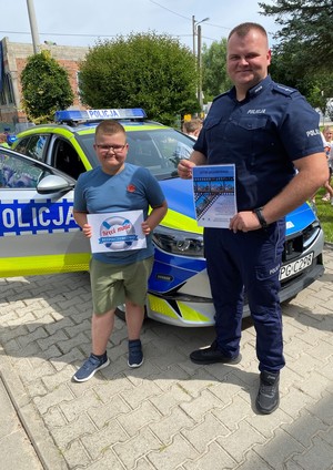umundurowany policjant z dzieckiem przed radiowozem trzymają promujące ulotki