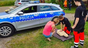 Bezpieczne wakacje uczennice uczą pierwszej pomocy kierującą w tle radiowóz