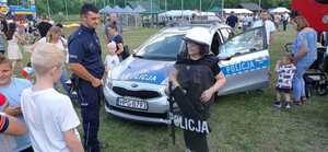 Umundurowany policjant oraz osoby biorące udział w akcji profilaktycznej. Na zdjęciu chłopiec trzymający tarczę z napisem Policja