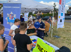 stoisko profilaktyczne przy którym stoja dzieci policjantka wiąże niebieksiego balona
