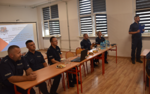 Umundurowani policjanci oraz ekran na którym znajduje się logo i temat debaty społecznej