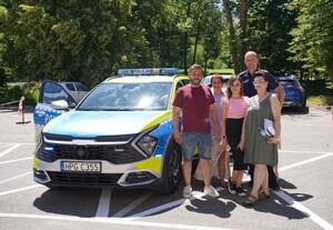 Dzielnicowy z organizatorami akcji Bezpieczne przygody  pozuje na tle oznakowanego radiowozu