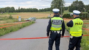 Dwóch umundurowanych policjantów ruchu drogowego zabezpieczających trasę rajdu. Są tyłem. Na drodze widać pojazd