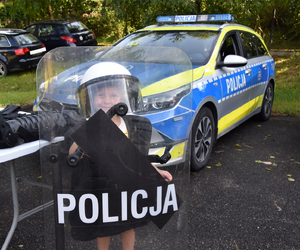 Dziecko trzymające tarczę z napisem POLICJA, stojące obok policyjnego radiowozu