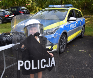 Dziecko trzymające tarczę z napisem POLICJA, stojące obok policyjnego radiowozu