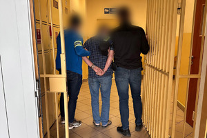 mężczyzna trzymany przez policjantów w pomieszczeniu dla osób zatrzymanych