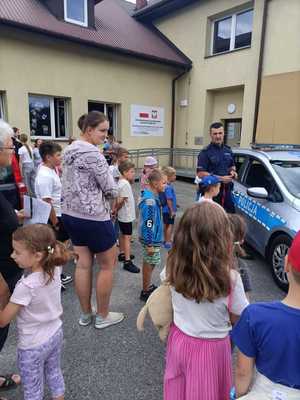 Umundurowany policjant oraz dzieci stojące przy policyjnym radiowozie