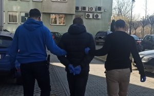 Dwójka policjantów w ubraniach cywilnych wyprowadza mężczyznę z rękami skutymi z tyłu