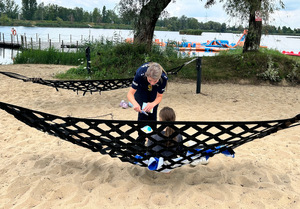 policjantka wręcza siedzącemu na hamaku dziecku ulotkę informacyjną