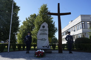 obelisk i krzyż z zapalonym zniczem i wiązanką
