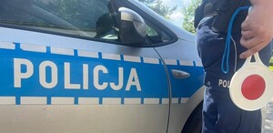Na tle radiowozu, policjant trzyma tarcze sygnalizacyjną