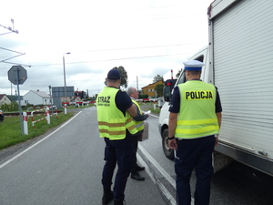 Dwóch strażników ochrony kolei, mężczyzna w stroju cywilnym, stoją obok samochodu