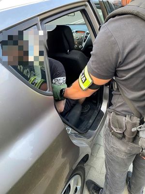 Policjant nieumundurowany, który trzyma zatrzymanego siedzącego w radiowozie