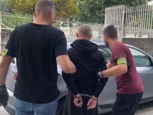 dwóch nieumundurowanych policjantów prowadzi zatrzymanego z kajdankami na rękach trzymanymi z tyłu do nieoznakowanego radiowozu