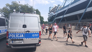 policyjne radiowozy stojące przy stadionie, obok których przechodzą kibice udający się na mecz