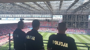 trzech umundurowanych policjantów obserwuje kibiców znajdujacych się na stadionie