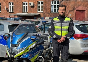 policjant krakowskiej drogówki stojący obok motocykla oraz radiowozów
