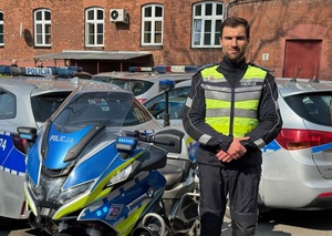 policjant krakowskiej drogówki stojący obok motocykla oraz radiowozów