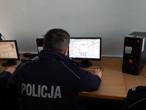 Policjant siedzi przy ekranie monitora i rysuje szkic miejsca zdarzenia drogowego.