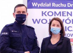 Na tle banneru Wydziału Ruchu Drogowego KWP w Krakowie stoi kobieta - szatynka oraz policjant.