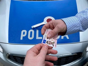przekazanie prawa jazdy z reki do ręki na tle napisu policja na radiowozie