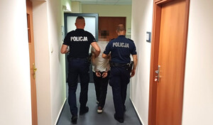 umundurowani policjanci prowadzą zatrzymanego mężczyznę korytarzem komisariatu