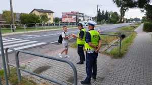 Dwóch policjantów stojących na chodniku i dziecko przechodzące przez przejście dla pieszych p